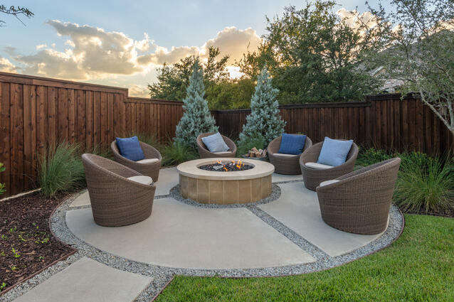 Backyard concrete patio firepit sitting area with chairs.