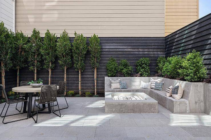 Concrete seating with firepit in the backyard with tables and chairs with privacy fence.